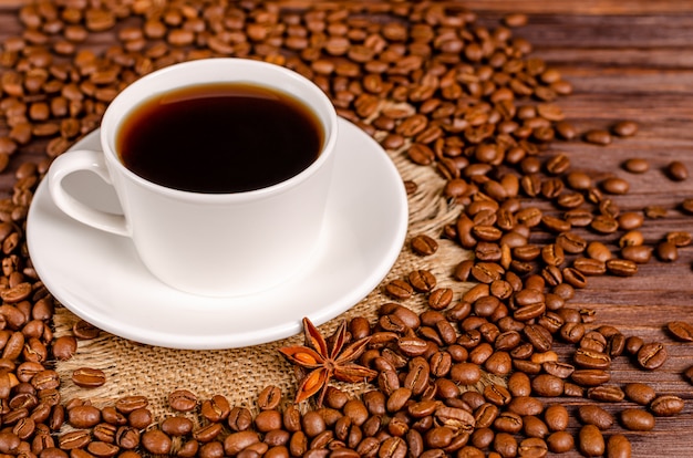 Une tasse de café aromatique noir dans une tasse blanche sur une table de grains de café torréfiés arabica café sur une table en bois