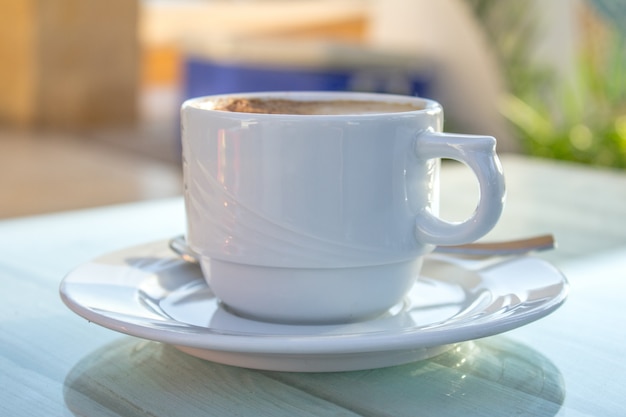 Tasse à café avec art au latte sur une table en bois blanche.