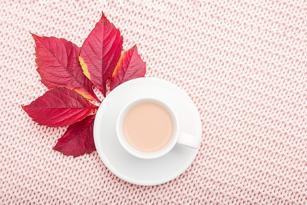 Tasse de café au lait et automne rouge laisse sur fond de plaid rose pastel.