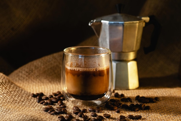 Une tasse de café au lait et une cafetière geyser sur fond de toile de jute sombre