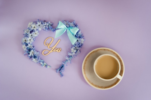 Tasse de café au lait et coeur faite de fleurs de jacinthe sur fond violet.