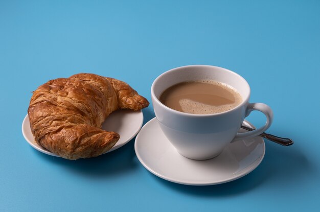 Tasse de café au lait et croissant sur fond bleu, copiez l'espace pour le texte.