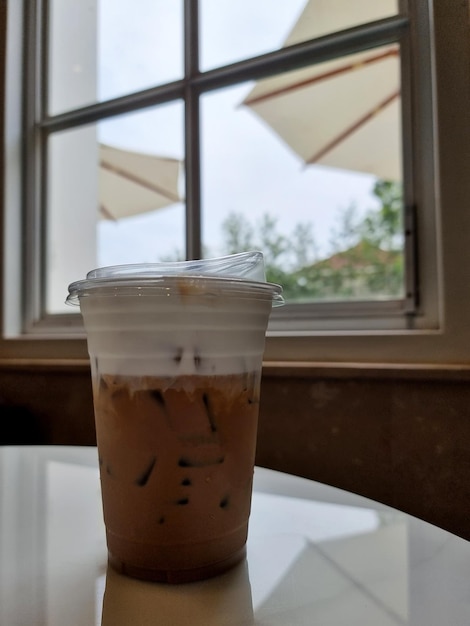 Une tasse de café au lait glacé sur la table et le fond de la fenêtre