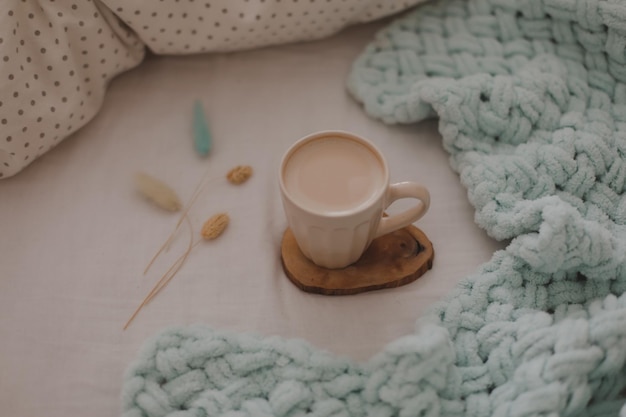 Tasse de café au lait sur le lit avec des draps blancs et une couverture Café du matin au lit concept