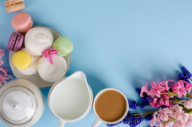 Tasse de café au lait, meringues blanches, macarons, pot de lait sur bleu pastel