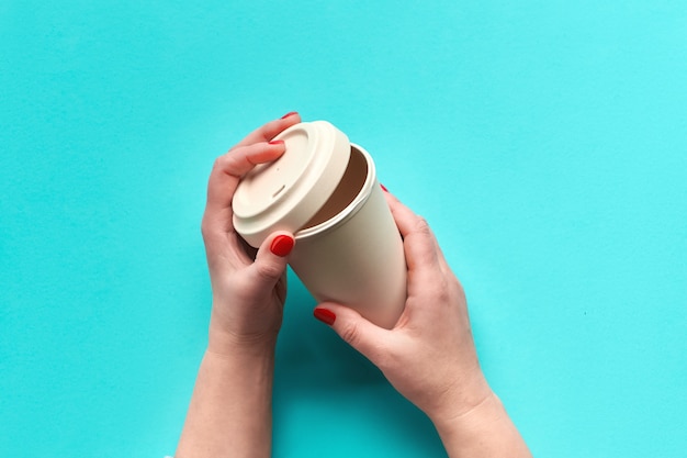 Tasse à café en bambou, garder la tasse ou tasse de voyage à la main féminine sur fond de menthe bleue. Mise à plat, image vue de dessus. Concept zéro déchet avec gobelet de voyage écologique.