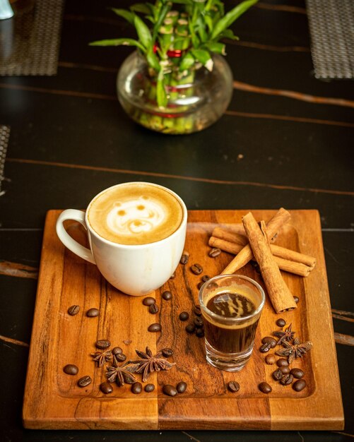 Une tasse de café avec des bâtons de cannelle et un verre de café sur un plateau en bois.