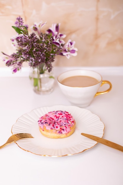 Tasse à café et beignet aux fraises sucrées sur plaque dorée avec bouquet de fleurs