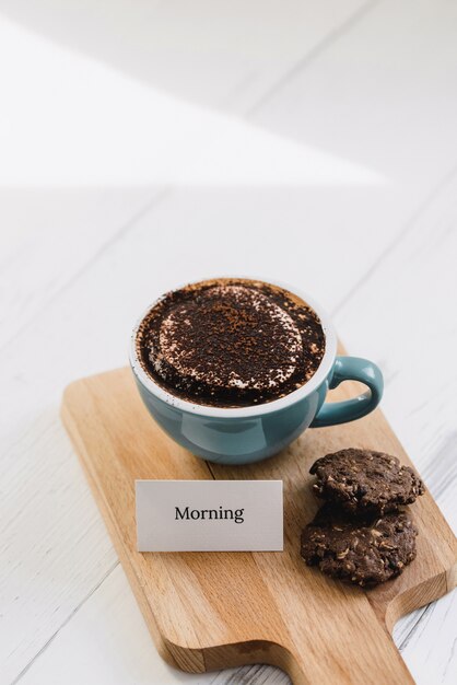 Tasse de café avec des biscuits au chocolat noir et un message d'accueil sur un plateau en bois au café