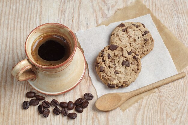 Tasse de café et biscuits au chocolat sur un papier placé sur une table en bois