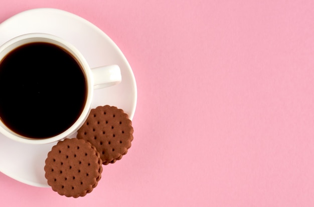 Tasse à café avec des biscuits sur une surface rose.