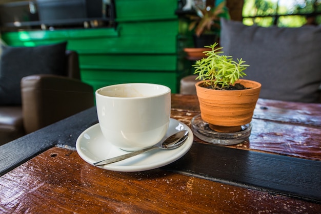 Une tasse de café blanc est placée sur une table en bois.