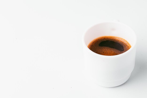 Une tasse de café blanche est posée sur une table blanche.