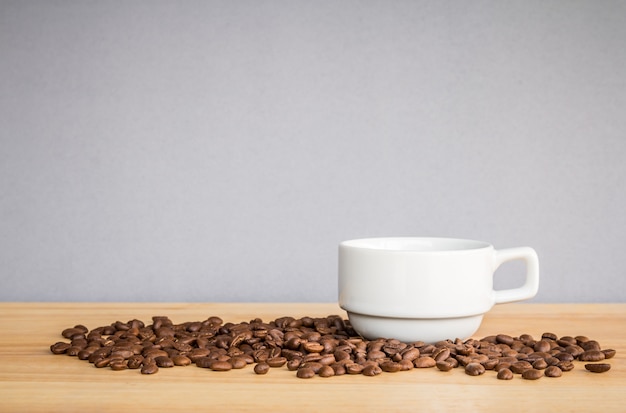 Tasse à café blanche et grains de café sur un bureau en bois avec fond gris