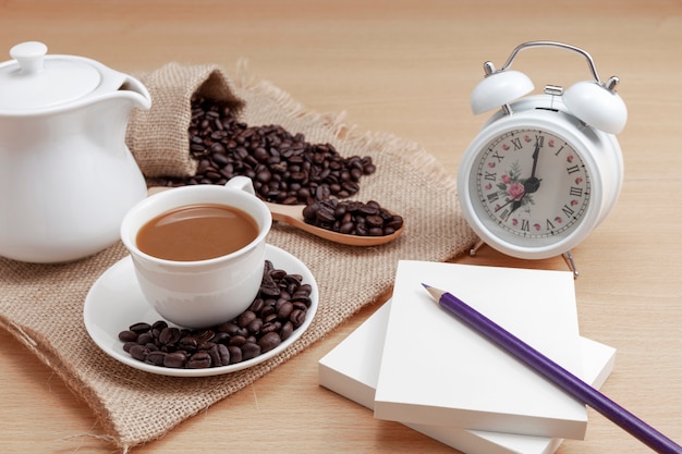 Tasse à café blanche avec grains de café et réveil sur fond en bois