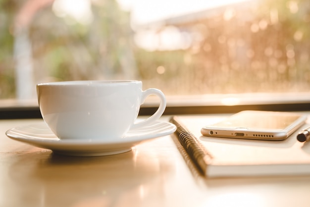 Tasse à café blanche en gros plan sur une table en bois près de la fenêtre avec une nuance claire sur la table au café. - Image