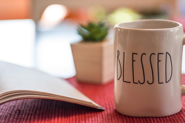 Photo une tasse à café blanche avec le mot « béni » est posée sur une table rouge.