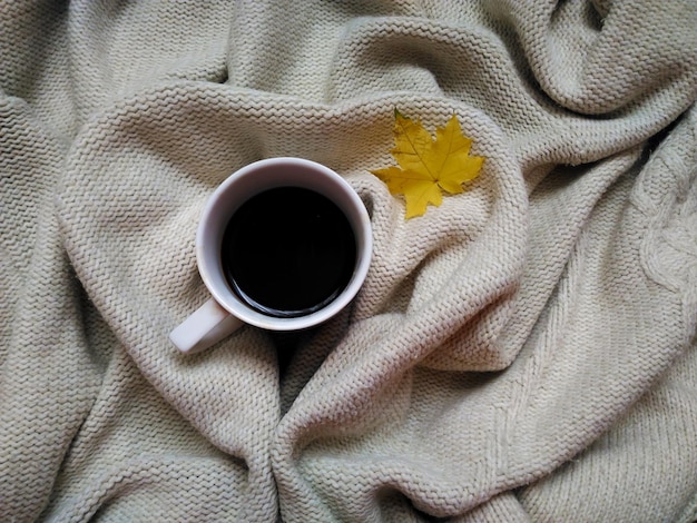 Tasse à café blanche avec reflet de feuille de coin dans la tasse. Sur fond tricoté beige