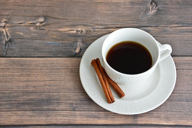 tasse de café blanche avec soucoupe et bâtons de cannelle isolés sur fond de bois