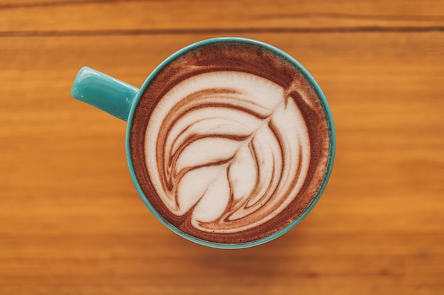 Tasse de café bleu avec plein d'art latte sur table en bois