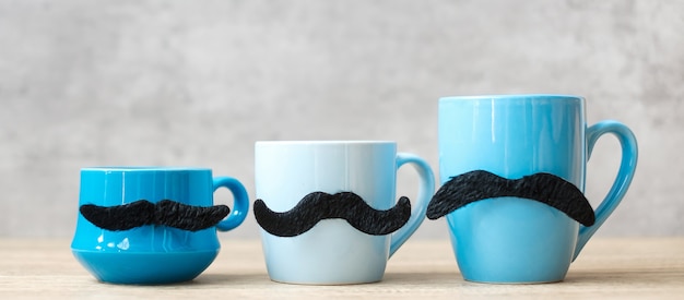 Tasse à café bleue et tasse à thé avec décor de moustache noire sur fond de table en bois le matin. Concept de novembre bleu, fête des pères heureux et journée internationale des hommes