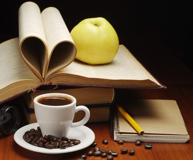 Tasse de café, bloc-notes, pomme et livre ouvert