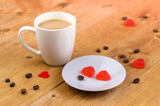 Une tasse de café et des bonbons en forme de cœur dans une assiette Sur une table en boisConcept romantique de la Saint-Valentin
