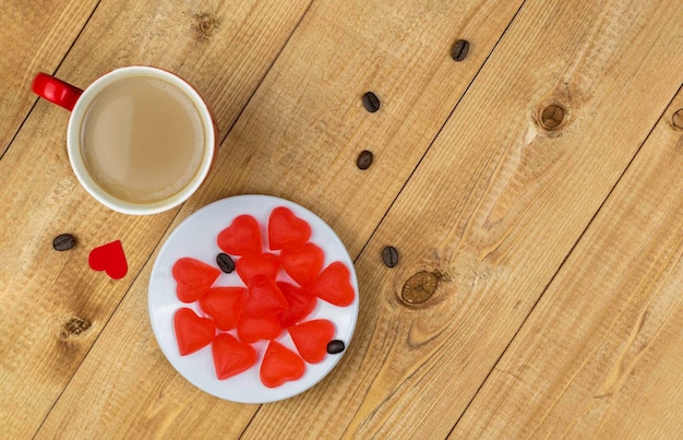 Une tasse de café et des bonbons en forme de coeur dans une assiette sur une table en boisRomantic St Valentines Day conceptFlat laycopy space