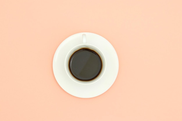 Une tasse de café avec un bord blanc est posée sur un fond rose.