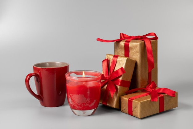 Une tasse de café, une bougie et des boîtes à cadeaux avec des rubans rouges sur un fond gris.