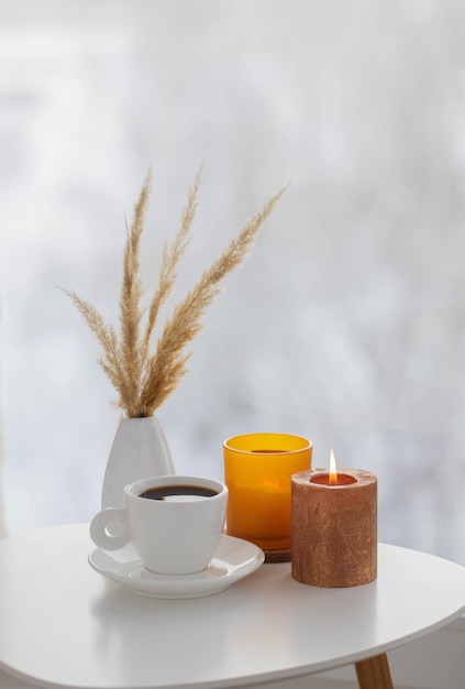 Tasse de café avec des bougies allumées sur une table blanche par fenêtre en hiver