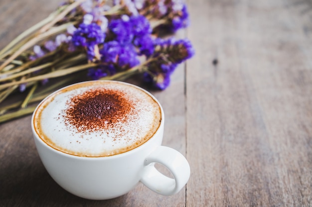 Une tasse de café avec bouquet de fleurs séchées violet sur fond de plancher en bois