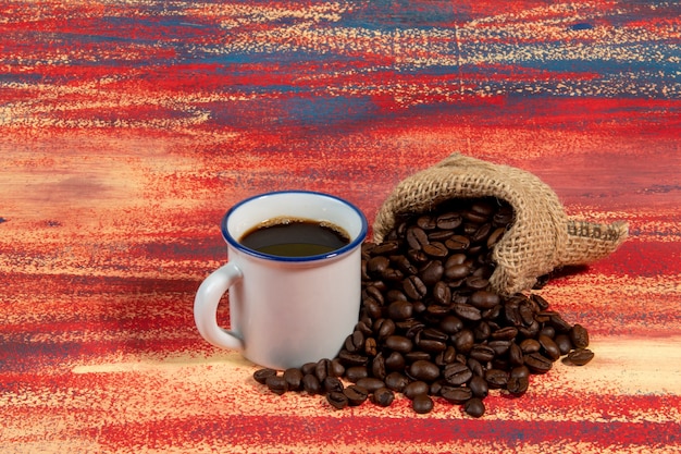 Tasse de café brésilien à côté d'un sac avec des grains torréfiés tombant dans une table rouillée