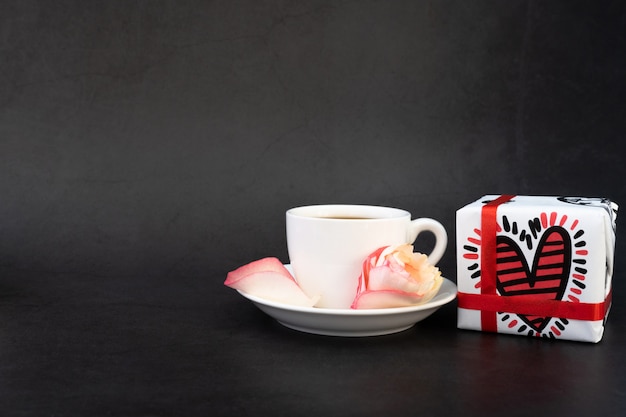 Tasse de café avec des cadeaux, des bonbons et des pétales de rose.