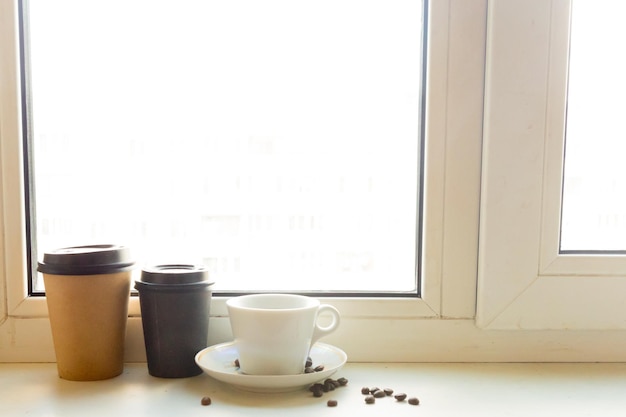 La tasse de café et le café à emporter sur le rebord de la fenêtre