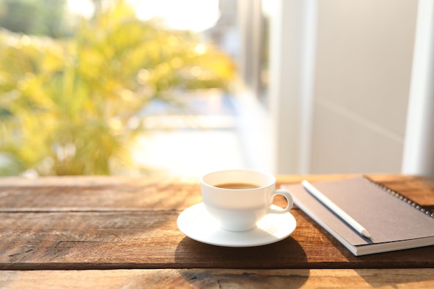 Une tasse de café, un cahier et un crayon sur une table en bois.