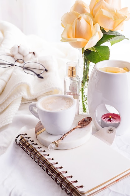 Une tasse de café sur le cahier, les roses, le verre et la bougie