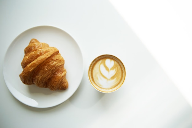 Tasse de café cappuccino et croissant sur table blanche, vue de dessus