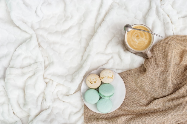 Tasse à café cappuccino et savoureux macarons sucrés sur fond clair avec espace de copie. Concept de matin d'hiver, le temps de se détendre. Vue de dessus. Mise à plat