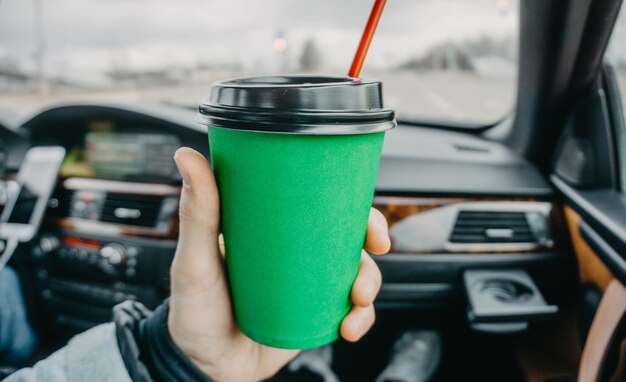 tasse de café en carton vert dans la voiture dans les mains boire pendant le voyage