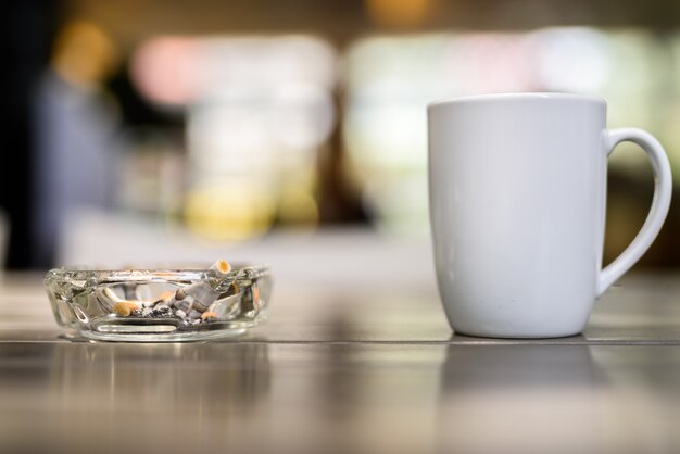 Tasse à café et cendrier avec des cigarettes sur une table en bois au restaurant