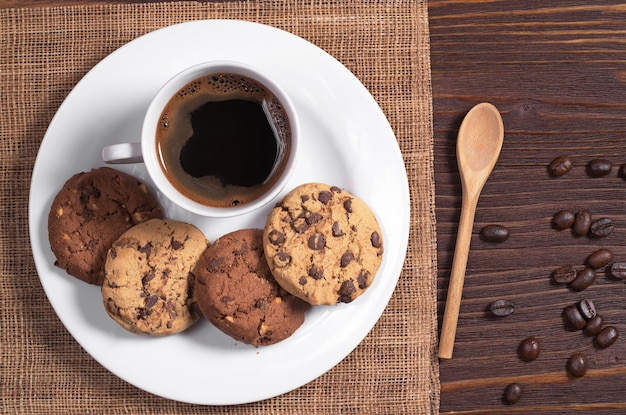 Tasse de café chaud et biscuits au chocolat et aux noix dans une assiette sur la vue de dessus de table en bois marron