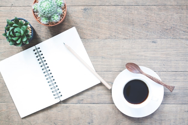 Une tasse de café chaud avec un carnet vide et un pot de cactus sur une table en bois avec un espace de copie