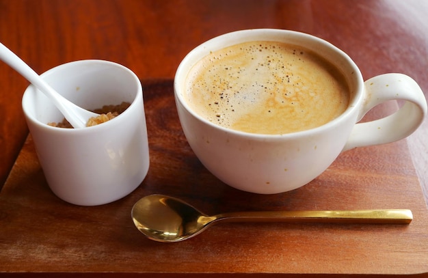 Une tasse de café chaud avec une cassonade et une cuillère à café en laiton sur une table en bois