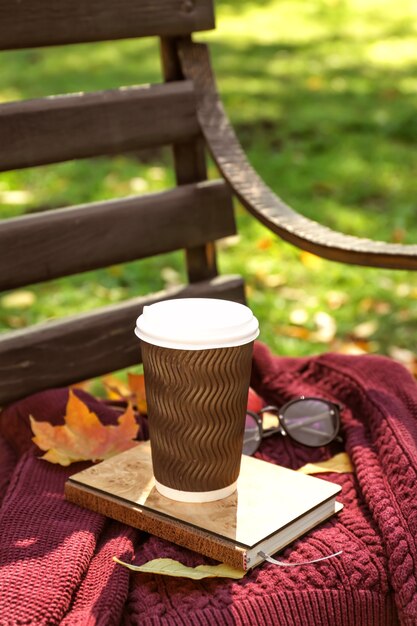 Tasse de café chaud avec chandail chaud et feuilles d'automne sur banc en bois dans le parc