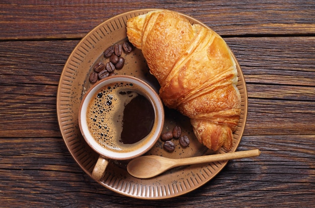 Tasse de café chaud et croissant dans une assiette sur une table en bois foncé, vue de dessus