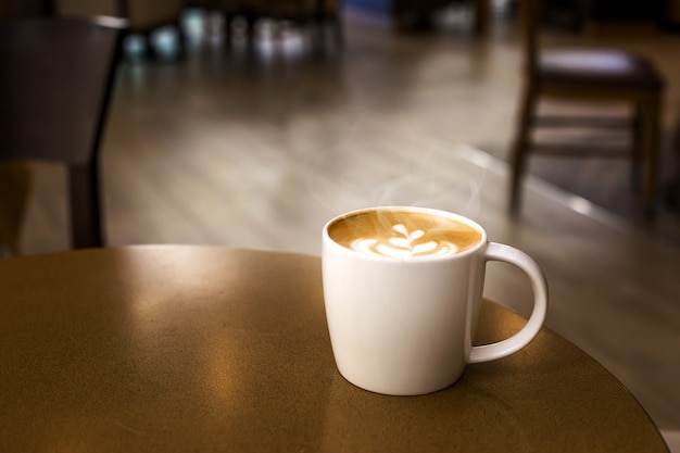 Tasse de café chaud avec de la fumée sur une table en bois dans un café vide