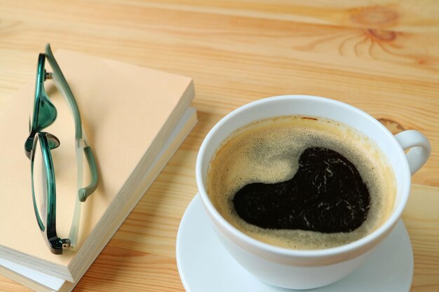 Tasse de café chaud avec de la mousse en forme de coeur sur une table en bois avec des livres et des verres