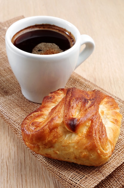 Tasse de café chaud et petit pain sur table en bois