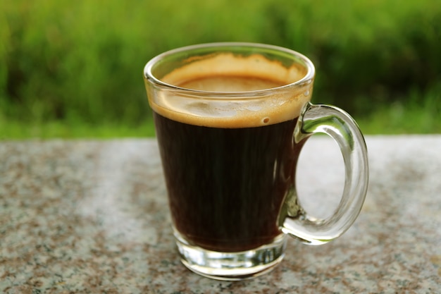 Tasse de café chaud sur la terrasse extérieure avec un buisson vert vibrant flou en arrière-plan